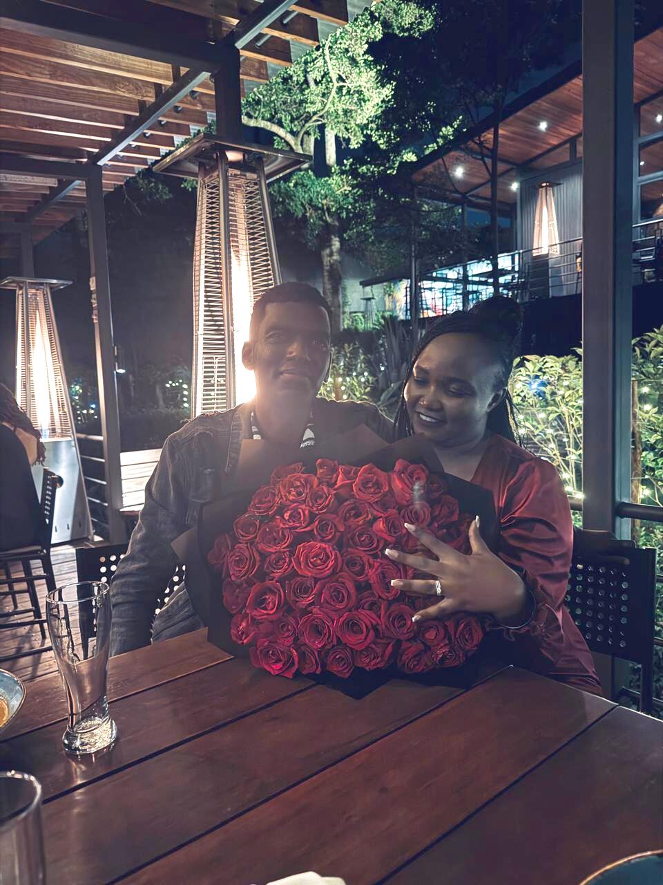 Shee showing her ring beside a large bouquet of red roses on the night of the proposal
